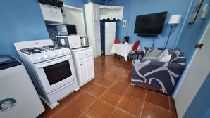 Cocina compacta con estufa, microondas y refrigerador. Cuenta con un pequeño comedor con mesa y sillas. Un televisor está montado en la pared.