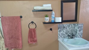 Un baño con pared color beige, un lavamanos con protector salpicadero de mármol y dos toalleros con toallas.