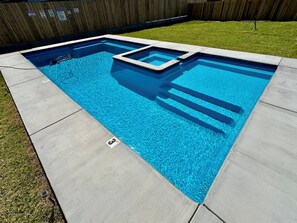 A rectangular swimming pool with a tiled deck, surrounded by a wooden fence and a grassy lawn. - HONEY HOLE with Pool and Hot Tub Bring Pets Add Fees (Port O'Connor)