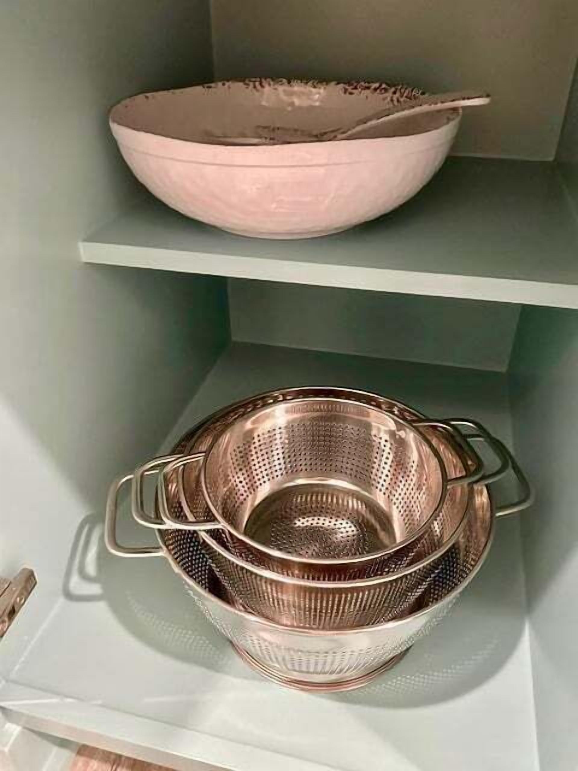 Una estant de cuina amb un bol rosa i un colador d'acer inoxidable.