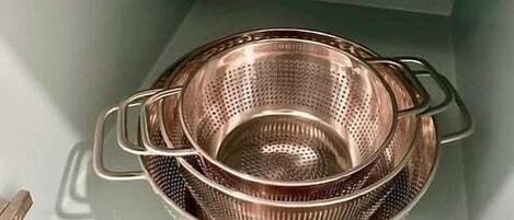 Una estant de cuina amb un bol rosa i un colador d'acer inoxidable.