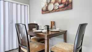 A dining area with a wooden table set for four, surrounded by upholstered chairs. A large decorative painting hangs above the table. - Stylish Haven NEW Walk to the Ocean, Smart TVs, Wifi (North Myrtle Beach)