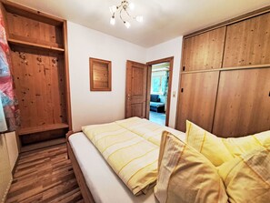 A bedroom with a bed, wooden wardrobe, and a small window.