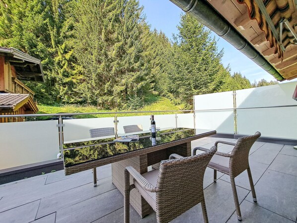 A balcony with wicker furniture, a glass table, and a bottle of wine.