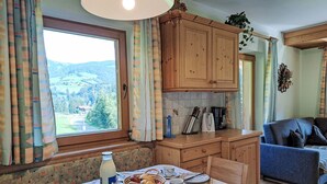 Une cuisine chaleureuse avec des meubles en bois, une table à manger dressée pour quatre personnes et une vue sur un paysage montagneux par la fenêtre.