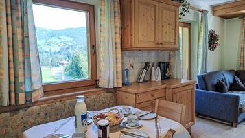 Une cuisine chaleureuse avec des meubles en bois, une table à manger dressée pour quatre personnes et une vue sur un paysage montagneux par la fenêtre.