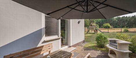 Un patio exterior con un banco de madera, una mesa y una parrilla.