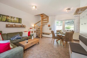 A modern living room with a sofa, coffee table, and dining area. A wooden staircase leads to an upper level.