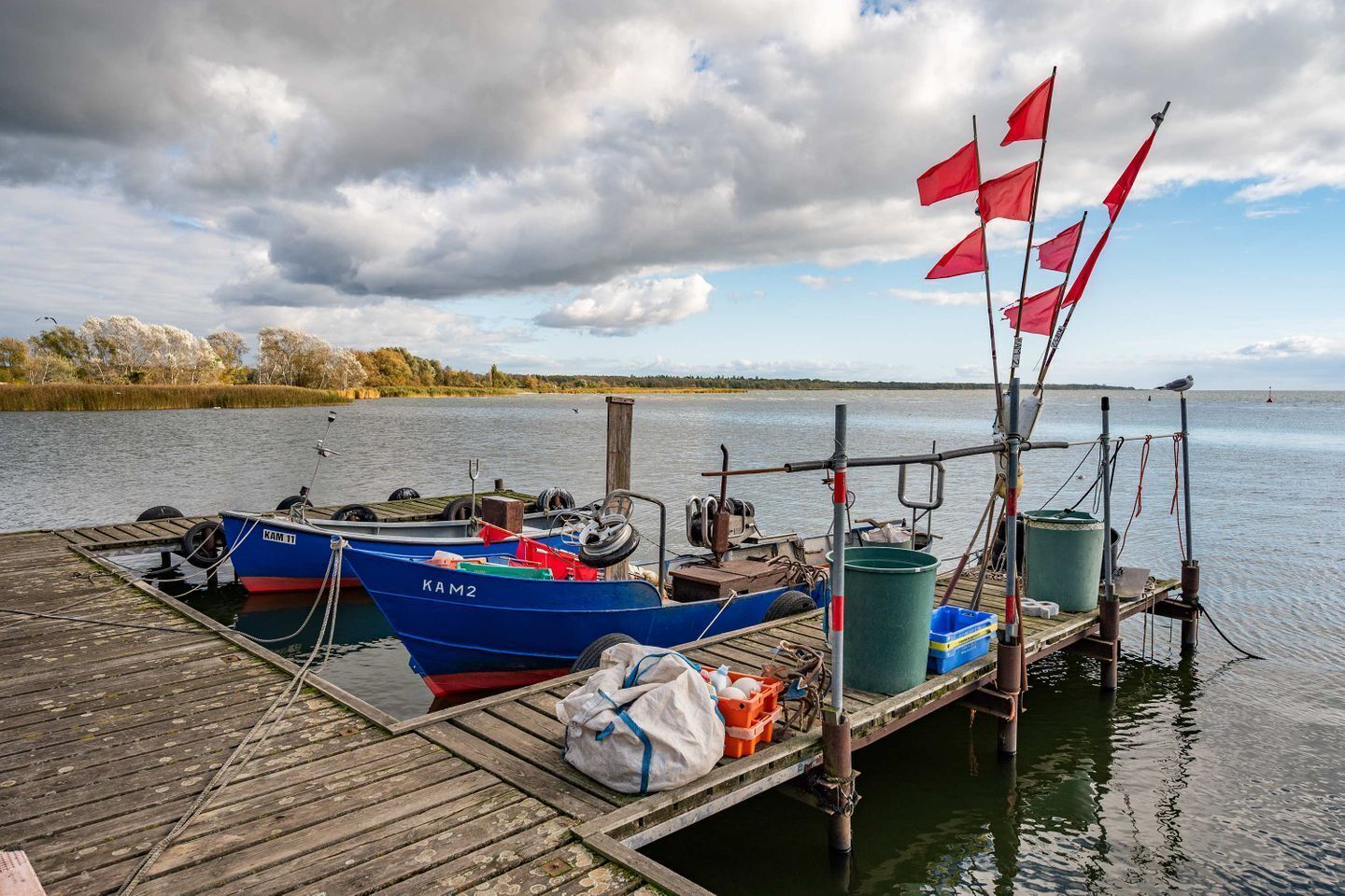 A wooden dock with two boats, a green barrel, and a white bag.