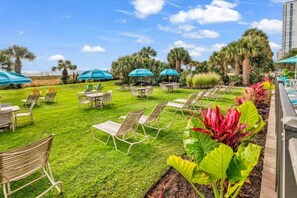 Un espace extérieur aménagé avec soin, comprenant une terrasse, des chaises et des tables, le tout entouré d’une végétation luxuriante et de palmiers.