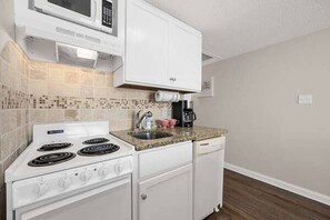 A compact kitchen with a stove, microwave, and coffee maker.