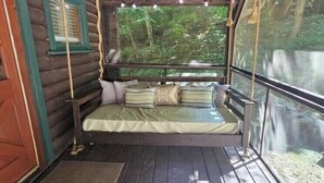 A wooden cabin with a swing bed, a window overlooking a forest, and a wooden deck. - Private couples retreat/pet friendly/early checkin (Pigeon Forge)