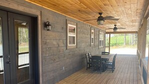 Una terraza cubierta de madera con mesa y sillas, un ventilador de techo y vistas al exterior.
