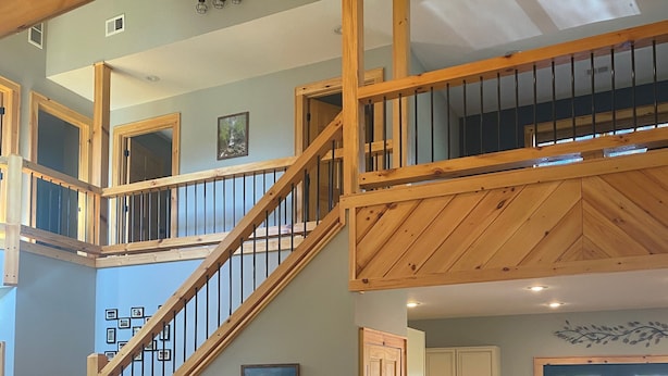 Un amplio espacio de sala con una escalera de madera, un sofá de cuero y una mesa de centro de vidrio.