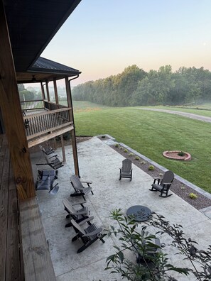 Een overdekt terras met buitenmeubilair en uitzicht op een grasveld.