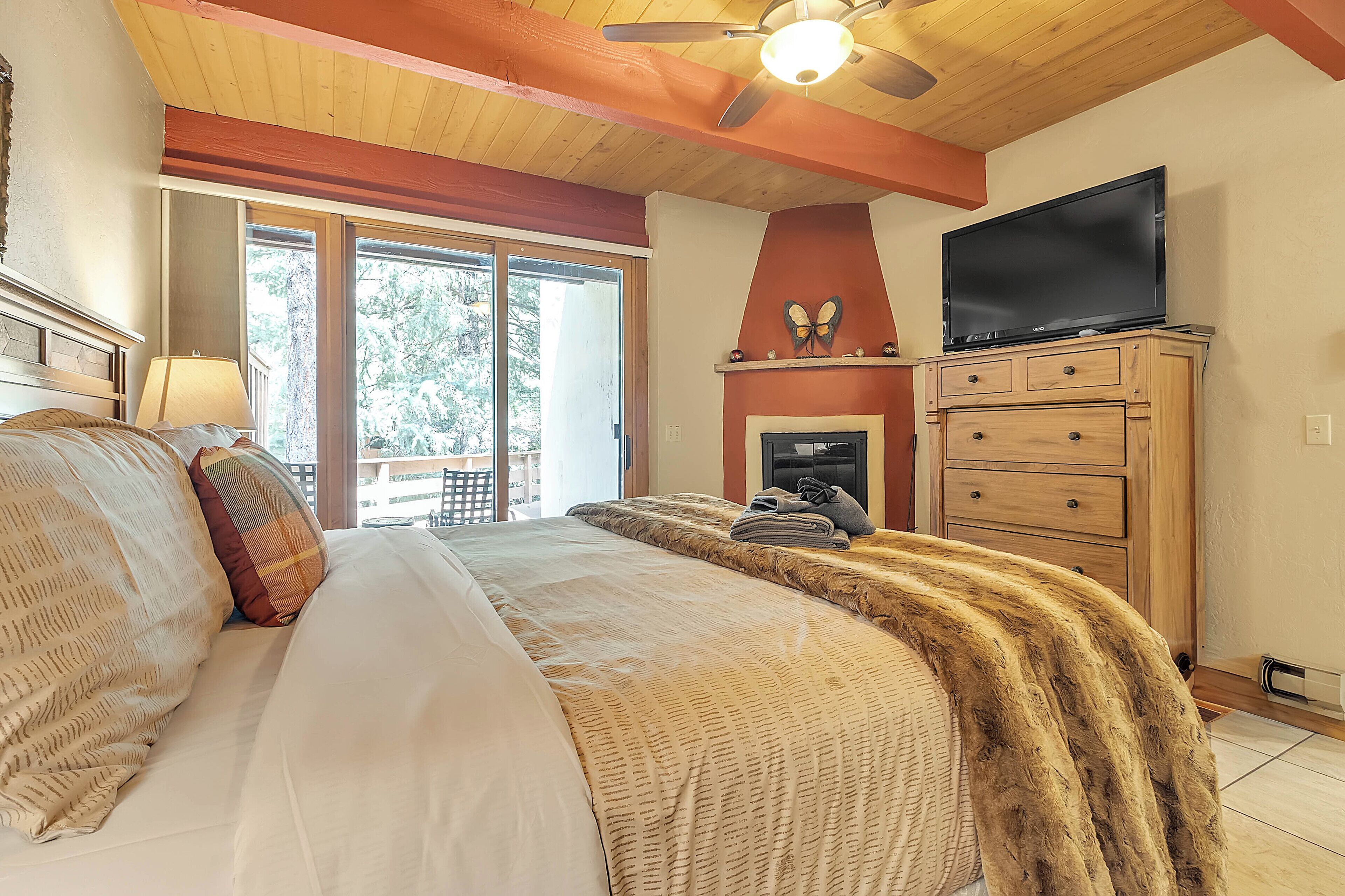 A bedroom with a large bed, a television, a fireplace, and a view of the outdoors.