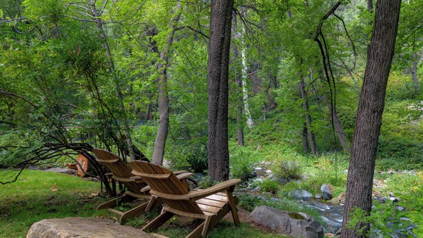Area boscosa con poltroncine Adirondack in legno e un piccolo ruscello.