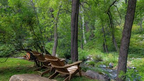 Area boscosa con poltroncine Adirondack in legno e un piccolo ruscello.