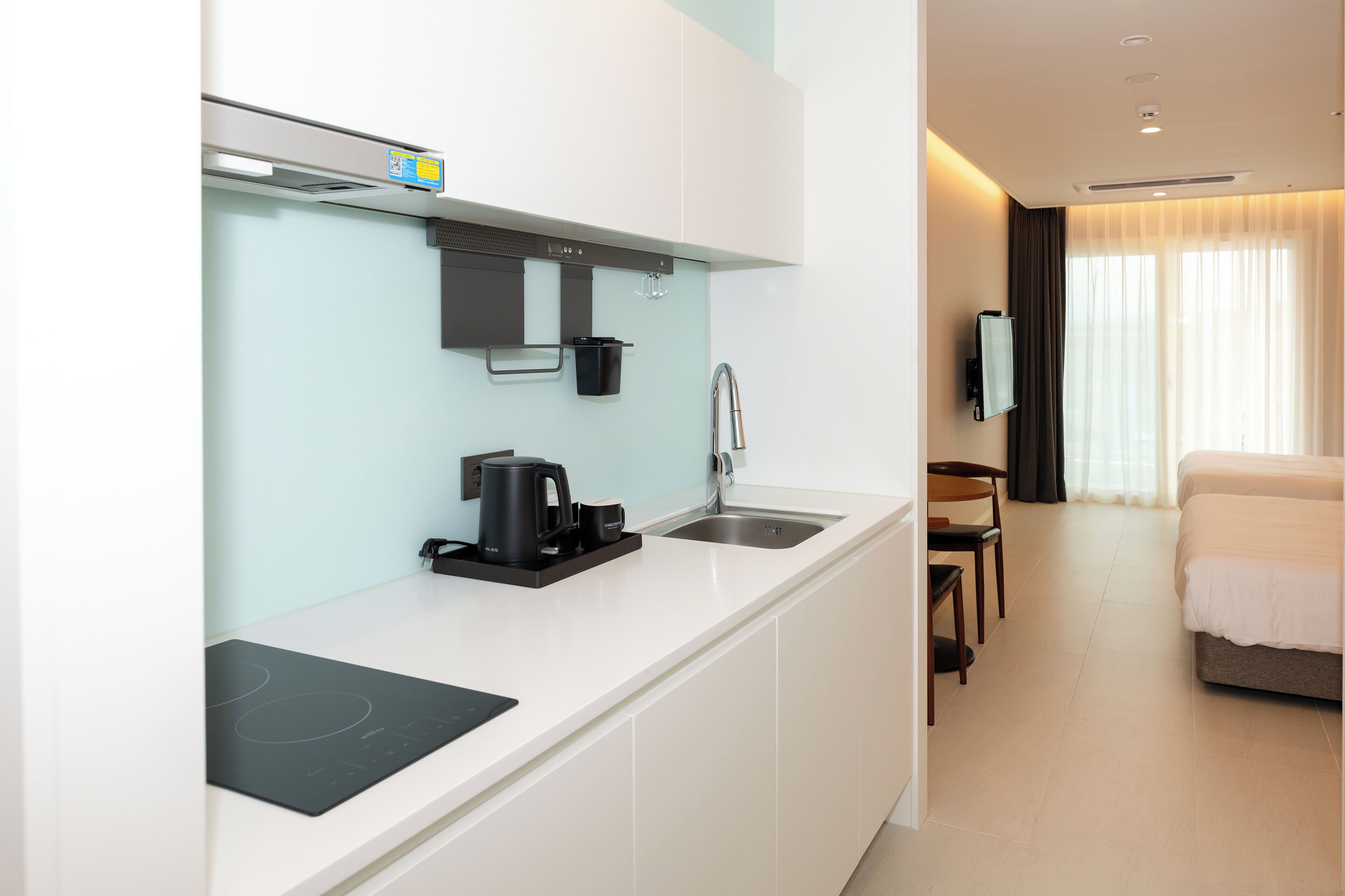 Habitación de hotel moderna con kitchenette, que incluye estufa, fregadero y cafetera. Hay una cama y un televisor en la habitación.