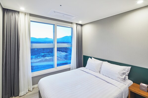 Una habitación de hotel con un ventanal grande, una cama y una mesita de noche.