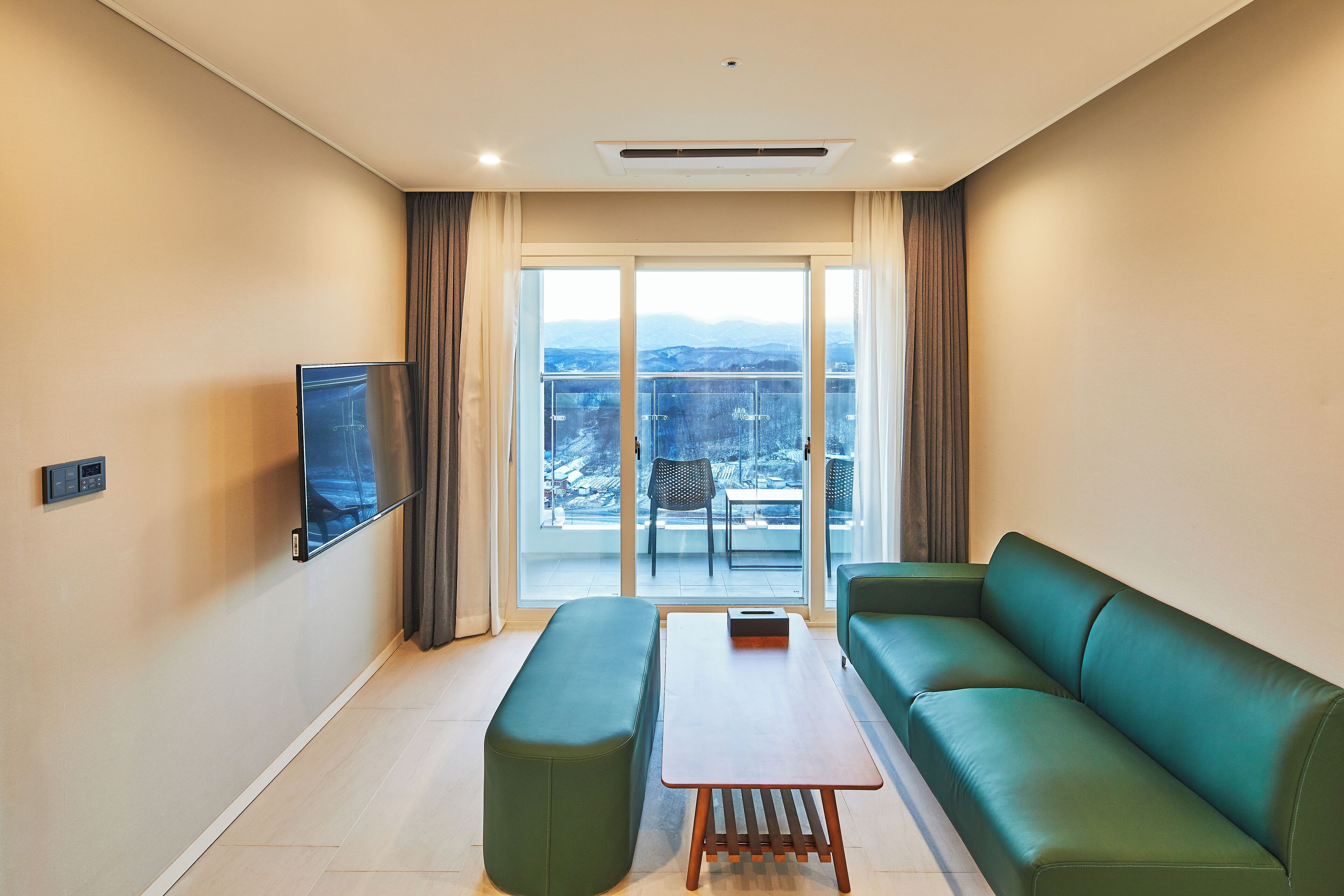 A modern living room with a green sofa, a wooden coffee table, and a flat-screen TV mounted on the wall.