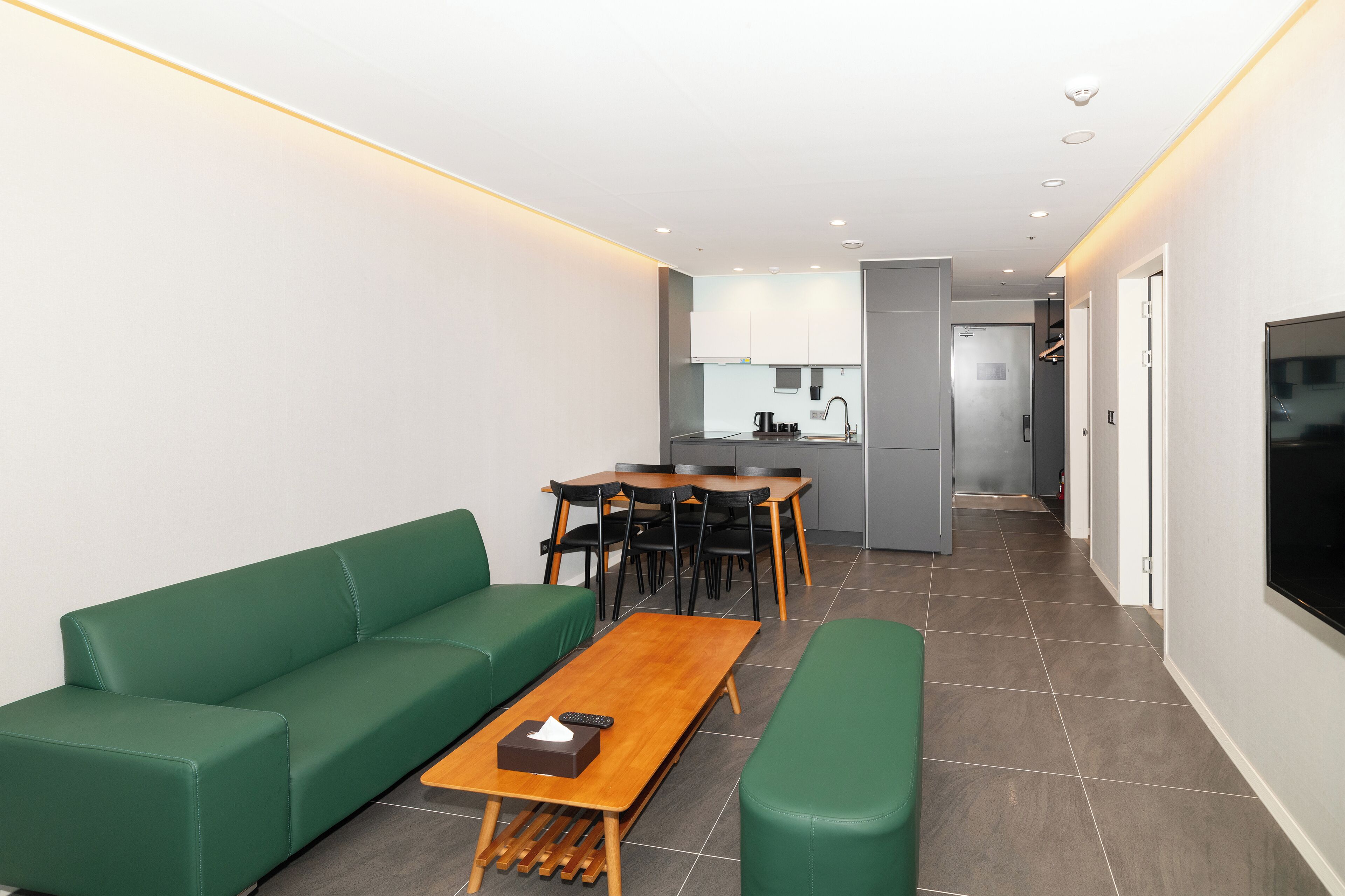 A modern living room with a green sofa, a wooden coffee table, and a dining area with a table and chairs.