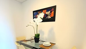 Un comedor moderno con una mesa de vidrio, dos sillas, una planta en maceta y una obra de arte enmarcada en la pared.