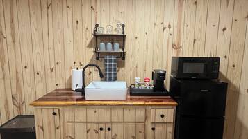 Cozinha com paredes e bancada de madeira, pia, cafeteira, micro-ondas e geladeira.