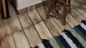 A dining area with a wooden table and chairs, a striped rug, and a wall-mounted shelf with plates and glasses. - Suit Aconchegante Rústica (Mairiporã)