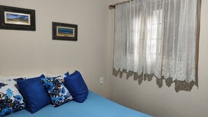 A bedroom with a bed, blue floral pillows, and two framed pictures on the wall. - Suit Aconchegante Rústica (Mairiporã)