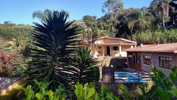 A house with a swimming pool, surrounded by lush greenery and trees. - Suit Aconchegante Rústica (Mairiporã)