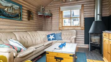 A cozy cabin interior with a leather sofa, a wooden chest, and a wood-burning stove.