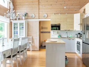 A modern kitchen with wooden cabinets, a central island, and a dining area with white chairs and a table. - Villa sirpia by Interhome (Lohja)