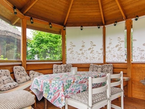 A covered outdoor seating area with a table and chairs, surrounded by wooden walls and windows with floral wallpaper. - Villa sirpia by Interhome (Lohja)