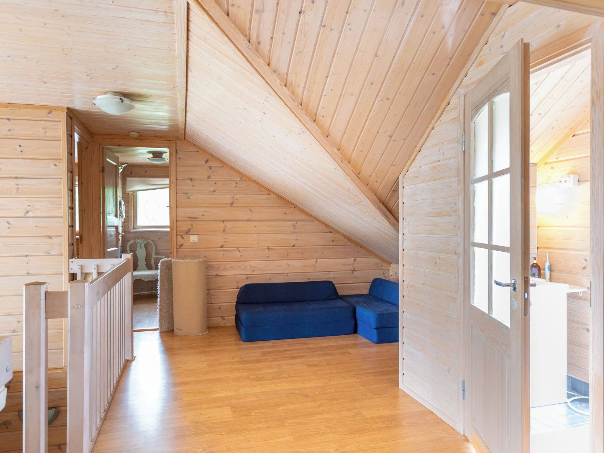 A wooden interior with a sloped ceiling, a blue sofa, and a door leading to a bathroom.