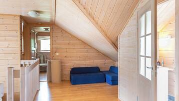 A wooden interior with a sloped ceiling, a blue sofa, and a door leading to a bathroom.