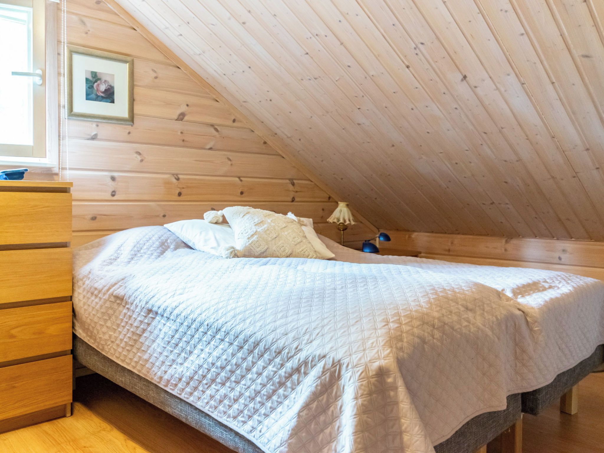 A bedroom with a wooden ceiling, a bed with a quilted bedspread, a dresser, and a picture on the wall.