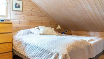 A bedroom with a wooden ceiling, a bed with a quilted bedspread, a dresser, and a picture on the wall.
