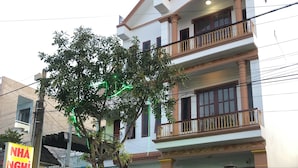 Ein zweigeschossiges Gebäude mit einem Balkon im zweiten Stock, einem schwarzen Metallzaun und einem Baum davor.