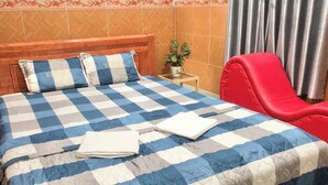 Ein Hotelzimmer mit kariertem Überwurf, einem roten Sessel, einem kleinen Tisch mit einer Pflanze und einem dekorativen Kopfteil.