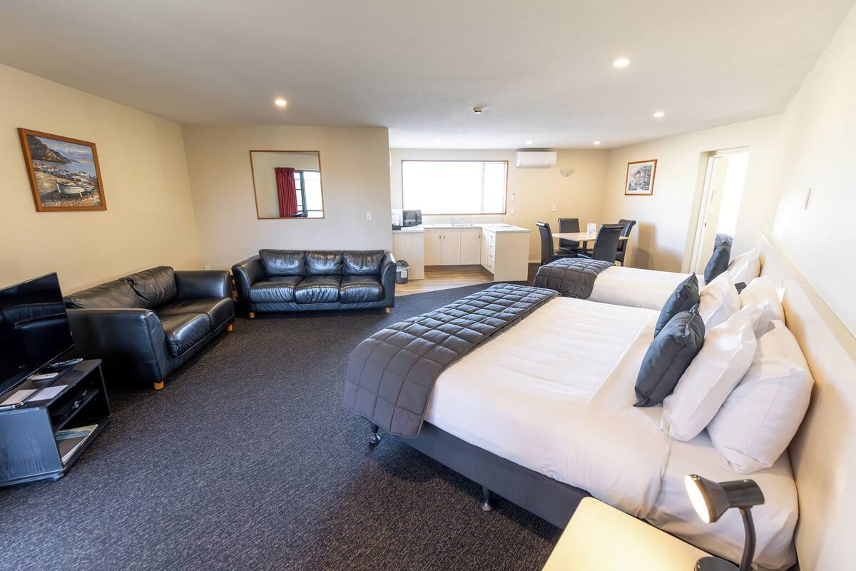 A hotel room with a large bed, a sofa, a desk, and a kitchenette.