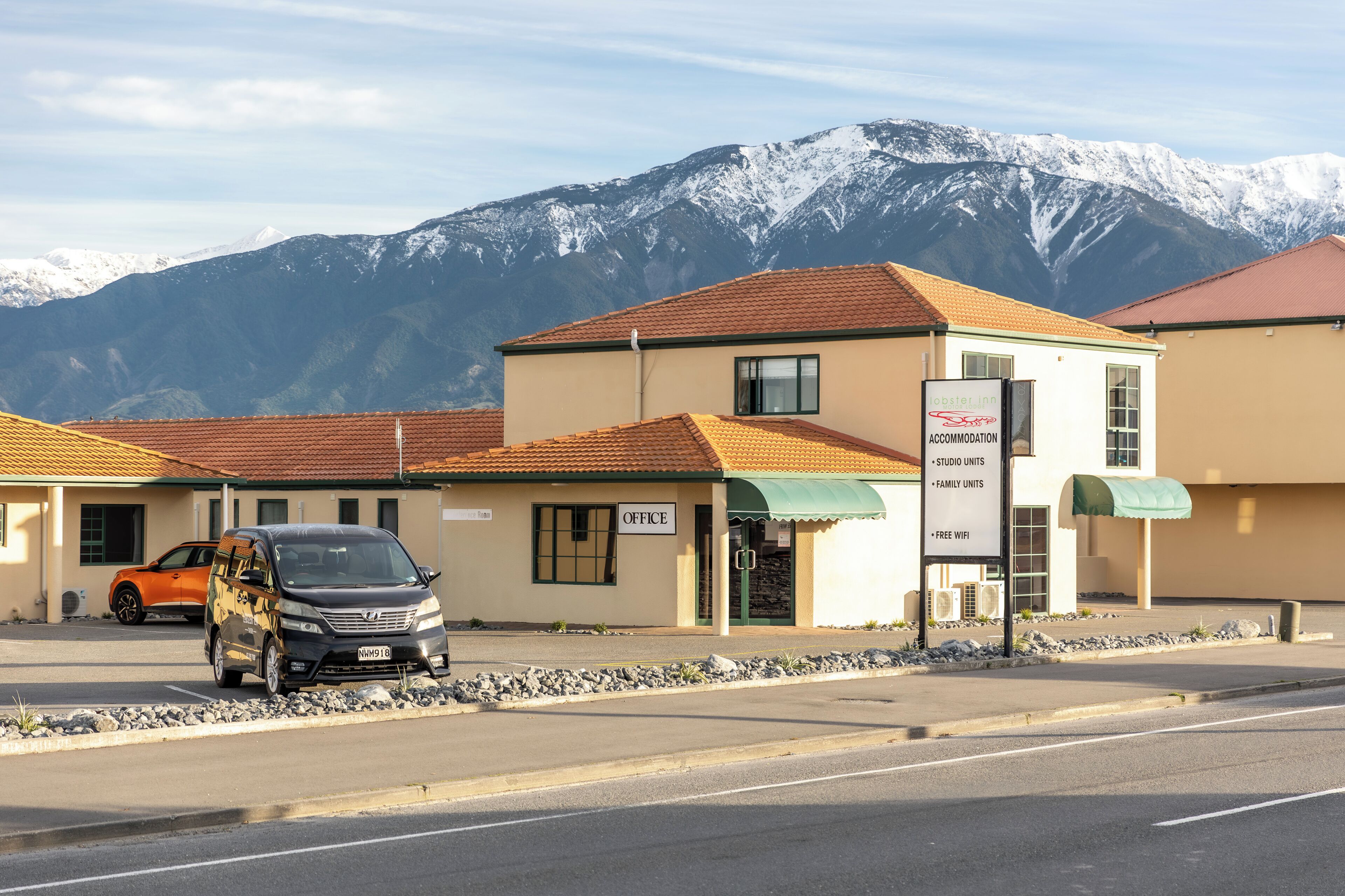 Un edificio con un letrero que indica que es un 'Master Inn', ofreciendo estudios y habitaciones familiares, con vistas a montañas nevadas al fondo.