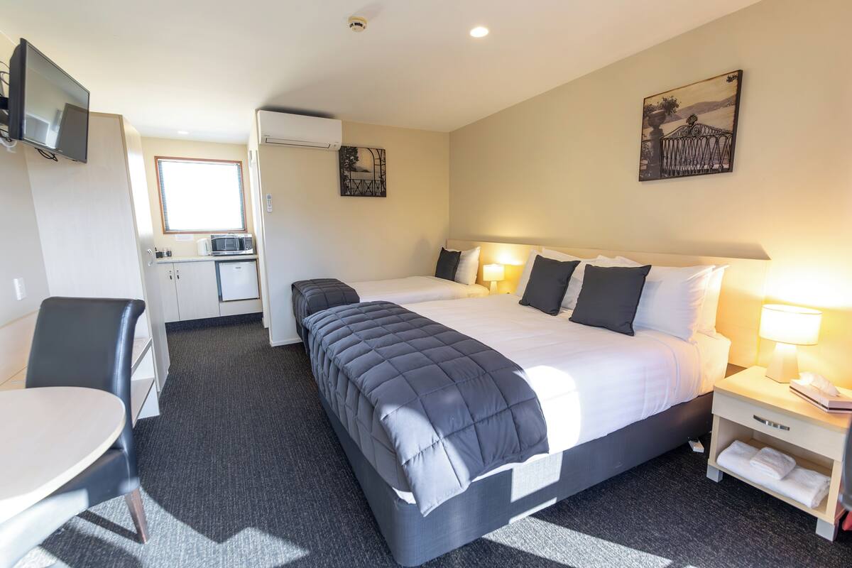 A hotel room with a bed, bedside table, lamp, and a small kitchenette.