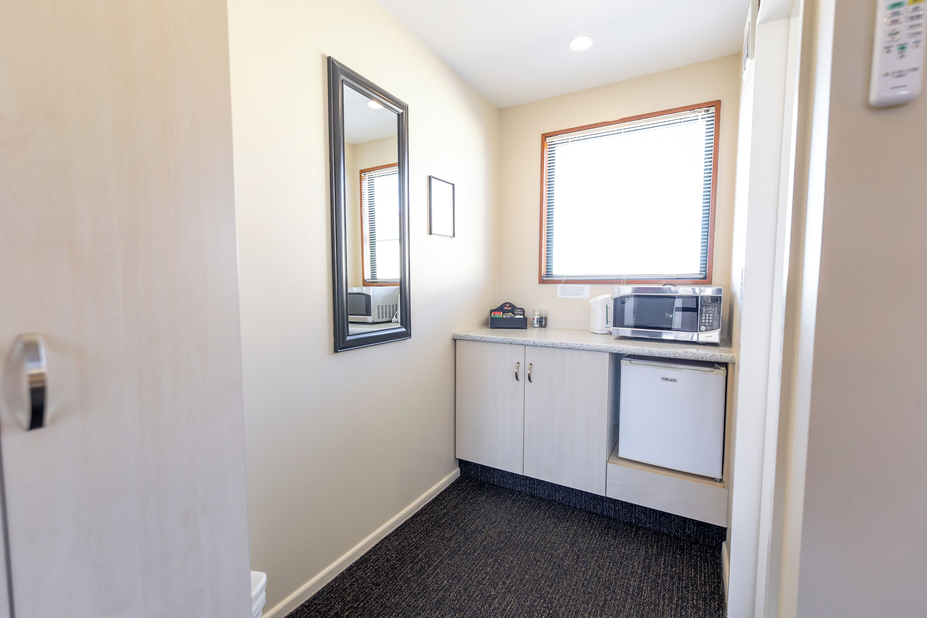 A small kitchenette with a microwave, refrigerator, and a framed picture on the wall.