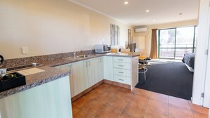 A modern kitchen with a granite countertop, white cabinets, and a black rug leading to a bedroom. - Lobster Inn Motel (Kaikoura)