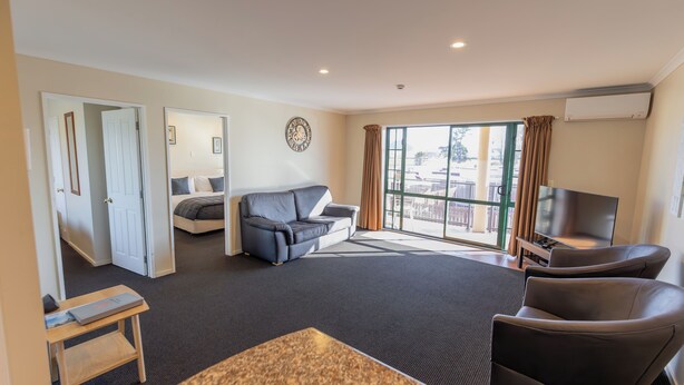 A modern living room with a sofa, a TV, and a view of the city through large windows. - Lobster Inn Motel (Kaikoura)