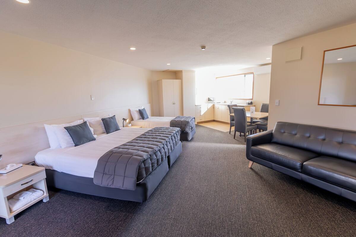 A hotel room with a large bed, a sofa, a desk, and a kitchenette.
