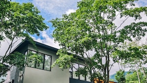 Uma casa moderna de dois andares com grandes janelas, rodeada por vegetação exuberante e árvores.