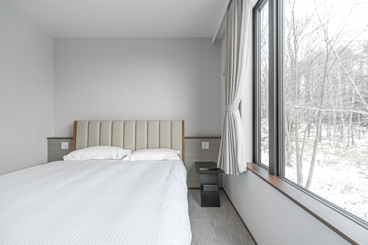 A modern bedroom with a large bed, a nightstand, and a window with curtains.