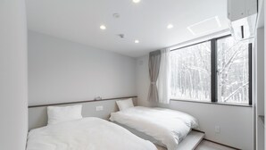 Quarto de hotel moderno com duas camas, uma janela grande com vista para árvores e um banco embutido.